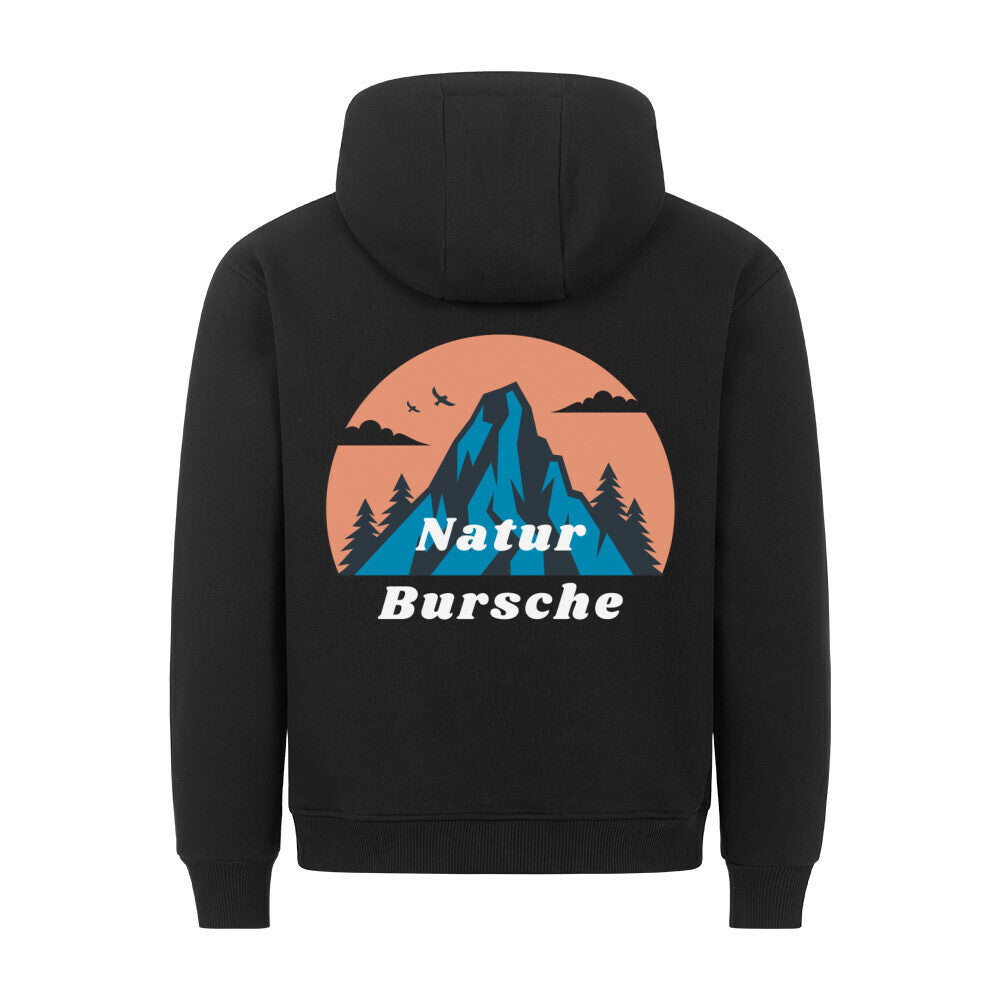 Der MarketPrint Premium Hoodie "Natur Bursche" in schwarz hat eine bequeme Passform und eine blaue Berg-, Tannenbaum-, Vogel- und Wolkengrafik auf einem orangefarbenen Kreis mit "Natur Bursche" in weiß. Hergestellt in Türkiye.