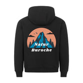 Der MarketPrint Premium Hoodie "Natur Bursche" in schwarz hat eine bequeme Passform und eine blaue Berg-, Tannenbaum-, Vogel- und Wolkengrafik auf einem orangefarbenen Kreis mit "Natur Bursche" in weiß. Hergestellt in Türkiye.