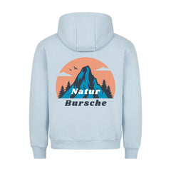Der MarketPrint Premium Hoodie "Natur Bursche" in hellblau hat eine lockere Passform und zeigt eine Berg-, Baum-, Vogel- und Wolkengrafik mit einem orangefarbenen Kreis auf dem Rücken sowie den Text "Natur Bursche". Hergestellt in Türkiye.