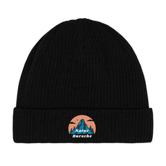 Die MarketPrint Beanie Mütze "Natur Bursche" ist eine schwarze, doppellagige Strick-Beanie mit Umschlag. Vorn ist ein Patch mit blauem Berg, Bäumen, Vögeln, orangefarbener Sonne und dem Schriftzug "Natur Bursche" in Weiß und Blau.