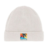 Die Beanie Mütze "Beach-Club" von MarketPrint ist aus weißer Bio-Baumwolle, doppellagig gestrickt und mit einem Patch verziert, der eine Palme, einen Sonnenuntergang und "BEACH-CLUB" in blauen Buchstaben zeigt.