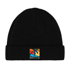 Die MarketPrint Beanie Mütze "Beach-Club" ist eine schwarze doppellagige Strick-Beanie mit Umschlag und rechteckigem Patch, das eine Palme vor buntem Sonnenuntergang sowie den Schriftzug BEACH-CLUB zeigt.