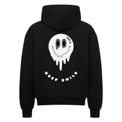 Der MarketPrint Oversized Zipper Hoodie "KEEP SMILE" in schwarz ist mit einem großen weißen, schmelzenden Smiley und "KEEP SMILE" auf dem Rücken bedruckt. Er besteht aus 100% Baumwolle für höchsten Tragekomfort und bietet eine stylische Oversized-Passform mit einem hochwertigen Reißverschluss.