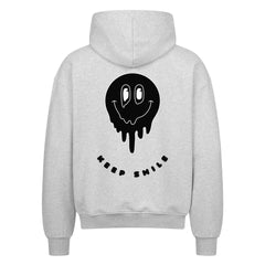 Der MarketPrint Oversized Zipper Hoodie "KEEP SMILE" ist ein graues Sweatshirt aus 100% Baumwolle mit einer schwarzen, schmelzenden Smiley-Grafik und dem Text "KEEP SMILE" auf dem Rücken.