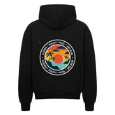 Der MarketPrint Oversized Zipper Hoodie "Urlaub" ist ein schwarzer Kapuzenpulli mit einer kreisförmigen Rückengrafik von Sonnenuntergang, Palmen und Wasser sowie "KOMM * MACH * MAL * URLAUB" am Rand. Er ist aus 100% Baumwolle gefertigt und bietet einen hohen Tragekomfort.