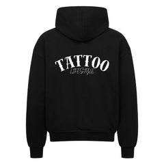 Der Oversized Zipper Hoodie "TATTOO" von MarketPrint ist schwarz, hat einen auffälligen weißen "TATTOO LIFESTYLE"-Druck auf dem Rücken und besteht aus 100% Baumwolle für hervorragenden Komfort und Stil.