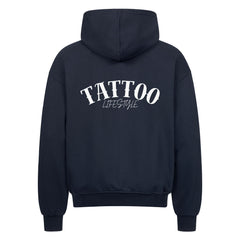 Der MarketPrint Oversized Zipper Hoodie "TATTOO" ist ein schwarzer Kapuzenpulli aus 100% Baumwolle mit langen Ärmeln und einer versteckten Tasche auf der Vorderseite. Auf der Rückseite befindet sich ein großer weißer "TATTOO LIFESTYLE" Druck.