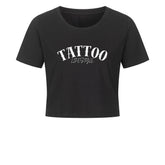Das MarketPrint Ladies Cropped "Tattoo" ist ein schwarzes, kurz geschnittenes Damen-Shirt aus Baumwolle mit weißem TATTOO LIFESTYLE Schriftzug auf der Brust, präsentiert vor weißem Hintergrund.