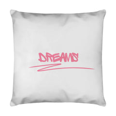 Das Kissen "DREAMS" von MarketPrint ist ein weißes quadratisches Kissen mit "DREAMS" in fetten rosa Graffiti-Buchstaben und einer rosa Unterstreichung, dazu herausnehmbares Futter und ein versteckter Reißverschluss für einfache Pflege.