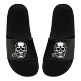 Die MarketPrint Badelatschen "Totenkopf" sind schwarze PVC-Rutschen mit einem Totenkopf und einer Zigarre auf jedem oberen Riemen - ideal für Ihren nächsten Badetag.
