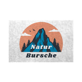 Die MarketPrint Fußmatte "Naturbursche" zeigt einen Berg mit Tannenbäumen, drei Vögeln und Wolken vor einer orangefarbenen Sonne. "Naturbursche" steht fett darunter auf dieser strapazierfähigen, schmutzabweisenden Matte.