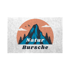 Die MarketPrint Fußmatte "Naturbursche" zeigt einen Berg mit Tannenbäumen, drei Vögeln und Wolken vor einer orangefarbenen Sonne. "Naturbursche" steht fett darunter auf dieser strapazierfähigen, schmutzabweisenden Matte.