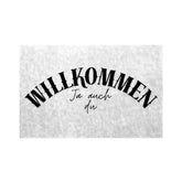 Die MarketPrint Fußmatte "Willkommen" zeigt schwarzen Text auf weißem Grund mit einem großen "WILLKOMMEN" und einem kleineren "Ja auch du" in Kursivschrift darunter. Das zentrierte, gewölbte Design macht diese Fußmatte sowohl einladend als auch langlebig.