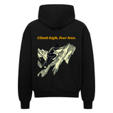 Der Oversized Zipper Hoodie "Climb high, fear less" von MarketPrint ist schwarz mit einer Bergsteiger-Grafik und einem gelben Slogan auf dem Rücken. Er ist aus 100% Baumwolle gefertigt und bietet hohen Tragekomfort.