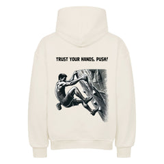 Der cremefarbene Oversized Hoodie "Bouldern" von MarketPrint zeigt eine Illustration vom Klettern mit "TRUST YOUR HANDS, PUSH!" über dem Bild.