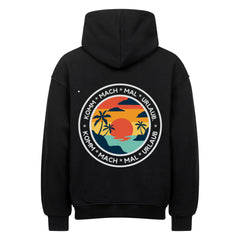 Der MarketPrint Oversized Hoodie "Urlaub" ist schwarz mit einem auffälligen, kreisförmigen Sonnenuntergang-, Meeres- und Palmenmotiv auf der Rückseite. Der Schriftzug "KOMM - MACH - MAL - URLAUB" umkreist die Grafik und sorgt für einen lässigen Style.