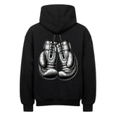 Der MarketPrint Oversized Hoodie "Boxhandschuhe" in Schwarz zeigt sich von hinten mit einer plakativen Illustration von zwei Boxhandschuhen in der Mitte, die an ihren Schnürsenkeln hängen.