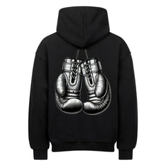 Der MarketPrint Oversized Hoodie "Boxhandschuhe" in Schwarz zeigt sich von hinten mit einer plakativen Illustration von zwei Boxhandschuhen in der Mitte, die an ihren Schnürsenkeln hängen.