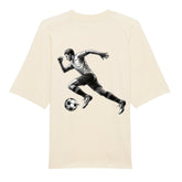 Das Premium Oversize Blast "Fußballer" T-Shirt von MarketPrint ist beige, aus Bio-Baumwolle mit kurzen Ärmeln und zeigt auf dem Rücken ein schwarz-weißes Grafikmotiv eines kickenden Fußballspielers.