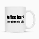 Die Infinity Merch Tasse "Kaffee" ist eine weiße Keramik Sublimationstasse mit schwarzem Text: "Kaffee leer? Baustelle steht still." Sie wird auf einem schlichten weißen Hintergrund dargestellt.