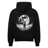 Der Oversized Zipper Hoodie "Astronaut" von Infinity Merch ist schwarz, besteht aus 100% Baumwolle und zeigt auf der Rückseite eine Grafik eines Astronauten auf dem Mond mit Sternen und Planeten im Hintergrund.