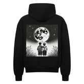 Der Oversized Zipper Hoodie Brüder-Mond von Infinity Merch ist aus 100% Baumwolle gefertigt und zeigt zwei Kinder, die in einer sternenklaren Nacht den Vollmond betrachten, mit hohem Gras im Vordergrund - perfekt in seiner übergroßen Passform.