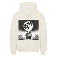 Der Oversized Hoodie "Brüder-Mond" von Infinity Merch ist cremefarben und zeigt auf der Rückseite eine schwarz-weiße Illustration von zwei Kindern, die nebeneinander den Vollmond am Sternenhimmel betrachten, umgeben von Gras.