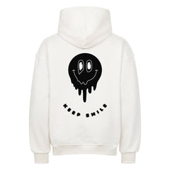 Der MarketPrint Oversized Hoodie "Keep Smile" in Weiß hat eine auffällige schwarze, schmelzende Smiley-Grafik und "KEEP SMILE" darunter auf dem Rücken.