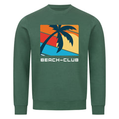 Das Premium Sweatshirt "Beach-Club" von MarketPrint ist ein grünes Unisex-Teil aus Bio-Baumwolle mit Palmenmotiv, geometrischem Sunset und BEACH-CLUB-Schriftzug - ideal für nachhaltige Mode-Fans.