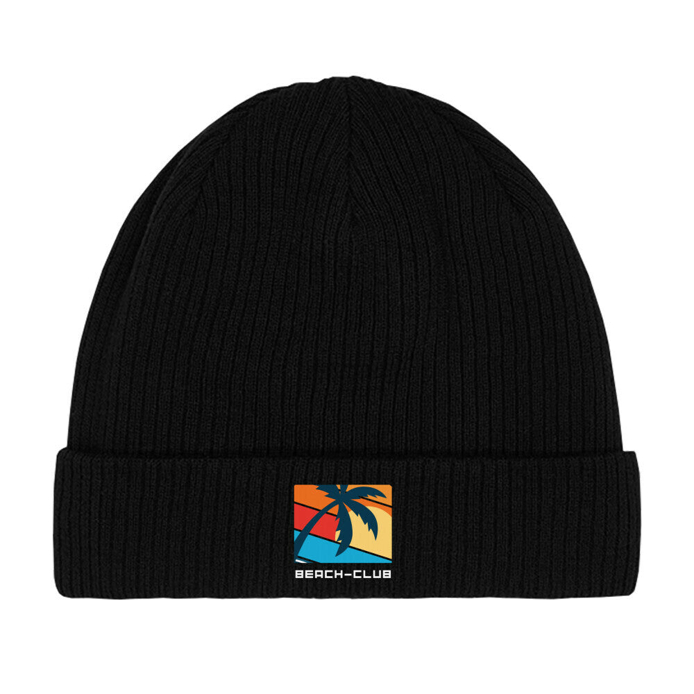 Die MarketPrint Beanie Mütze "Beach-Club" ist eine schwarze doppellagige Strick-Beanie mit Umschlag und rechteckigem Patch, das eine Palme vor buntem Sonnenuntergang sowie den Schriftzug BEACH-CLUB zeigt.