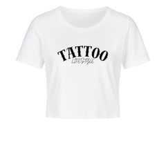 Das MarketPrint Ladies Cropped "Tattoo" Shirt ist ein weißes, kurz geschnittenes Damen-Shirt aus Baumwolle mit "TATTOO LIFESTYLE" in schwarzer Schrift vorne, präsentiert vor schlichtem weißen Hintergrund.