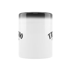 Die MarketPrint Zaubertasse "TATTOO" ist eine weiße keramische magische Tasse mit schwarzem Rand und stilisiertem schwarzem Text auf jeder Seite, die vor einem schlichten weißen Hintergrund steht.