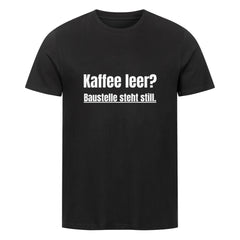 Das MarketPrint Premium Shirt "Steht Still" ist ein schwarzes Unisex-T-Shirt aus weicher Bio-Baumwolle (Single-Jersey) mit weißem Text: Kaffee leer? Baustelle steht still. Dargestellt auf einem schlichten weißen Hintergrund.