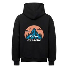 Der MarketPrint Oversized Hoodie "Natur Bursche" zeigt eine Rückengrafik mit einem blauen Berg, Bäumen und Vögeln vor einem orangefarbenen Kreis, darunter steht in weißer Schrift "Natur Bursche".