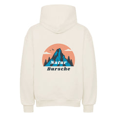 Der MarketPrint Oversized Hoodie "Natur Bursche" ist cremefarben und zeigt auf dem Rücken eine Berg-, Baum-, Vogel- und Wolkengrafik, darunter ist "Natur Bursche" in blau und weiß aufgedruckt.