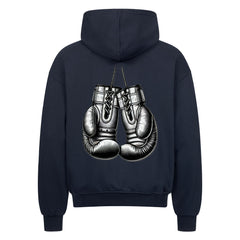 Der Oversized Zipper Hoodie "Boxhandschuhe" von MarketPrint ist ein schwarzer Premium-Kapuzenpullover aus 100% Baumwolle mit einem übergroßen Schnitt und einer Grafik von zwei Boxhandschuhen, die an den Schnürsenkeln auf dem Rücken hängen.