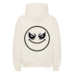 Der Oversized Hoodie "Böser-smiley" von MarketPrint ist cremefarben und zeigt ein großes, schwarz umrandetes, kreisrundes Smiley-Gesicht mit gewölbten Augenbrauen und einem verschmitzten, schelmischen Ausdruck auf dem Rücken.