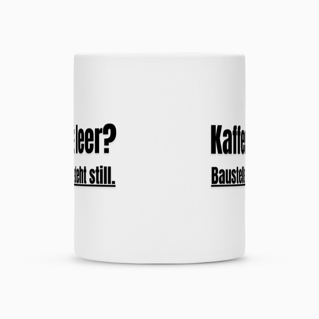 Eine weiße Sublimationstasse "Kaffee" von Infinity Merch mit Duraglaze-Beschichtung zeigt teilweise fett schwarzen deutschen Text wie "Kaffee", "leer?" und "asteht still.", sichtbar durch den Winkel.
