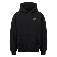 Der Infinity Merch Oversized Hoodie "Strand" ist ein hochwertiger schwarzer Kapuzenpulli mit einer Fronttasche und einer kleinen weißen Palme auf der linken Brust. Er ist aus schwerer Baumwolle gefertigt, die für Komfort und Haltbarkeit sorgt.