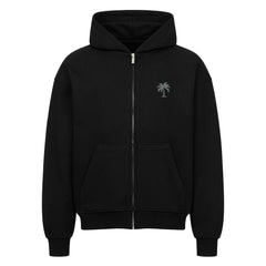 Der Oversized Zipper Hoodie "Strand" von Infinity Merch ist ein schwarzer Premium-Kapuzenpullover mit einer Fronttasche und einer kleinen Palmengrafik auf der linken Brust. Er besteht aus 100% Baumwolle und ist auf weißem Hintergrund abgebildet.